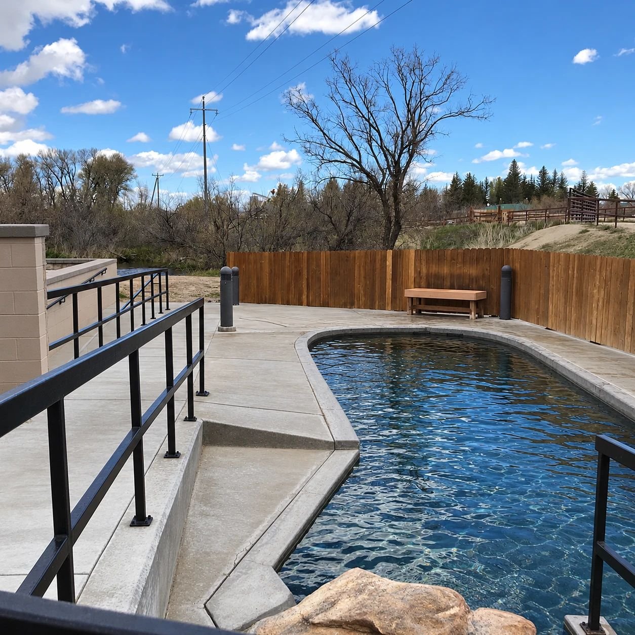 A long curving soaking pool with benches and railings beside the river